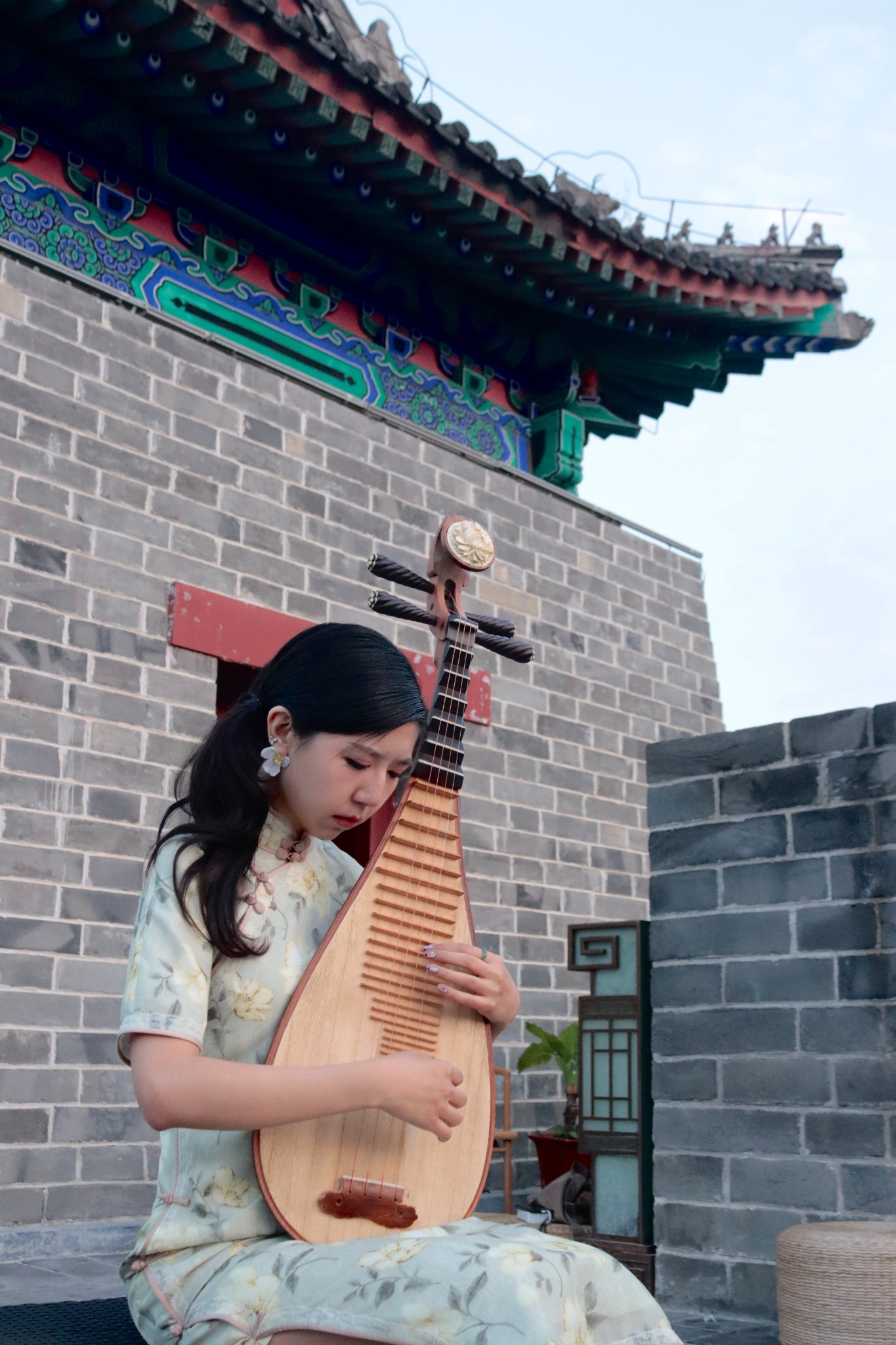 Xu Chang seated with her pipa in a courtyard beneath a tiled roof